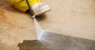 Maintenance worker cleaning dirty driveway with a pressure washer